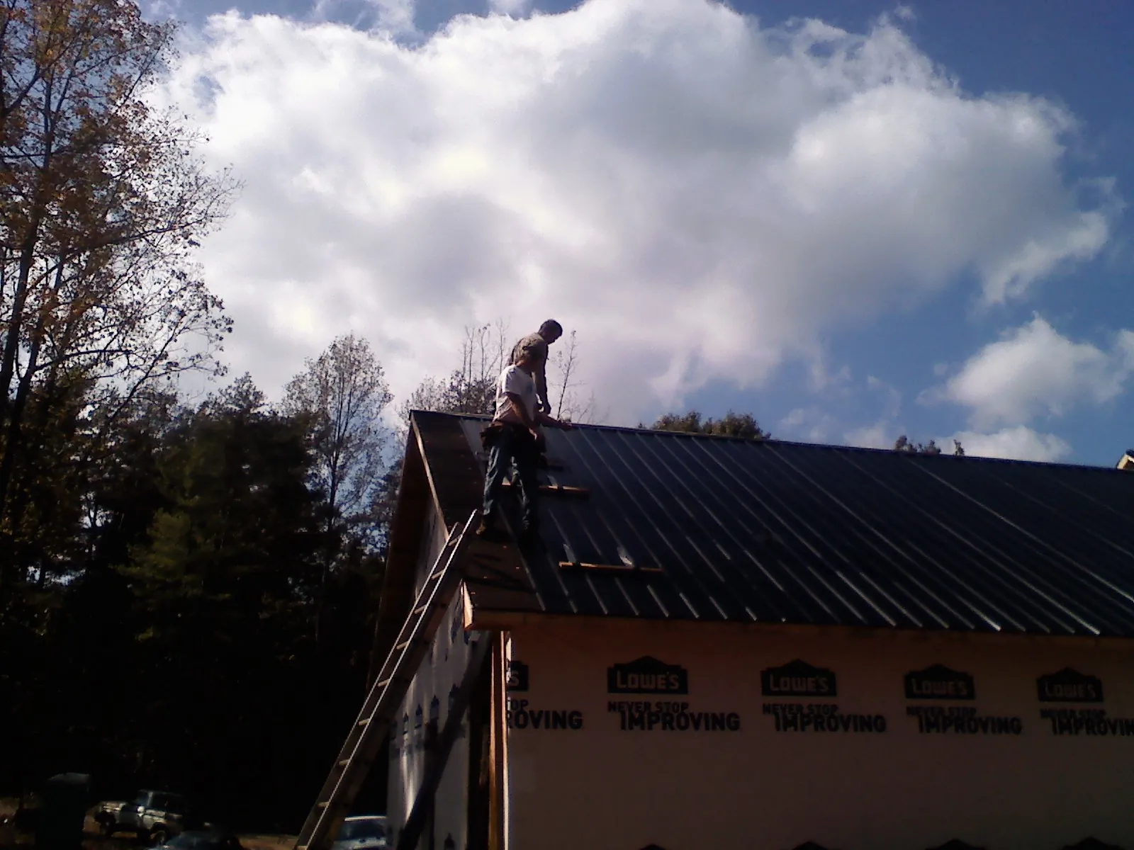 Roofer fastening dark metal panels high against a cloudy sky, from a Roof Inspection job in Windham